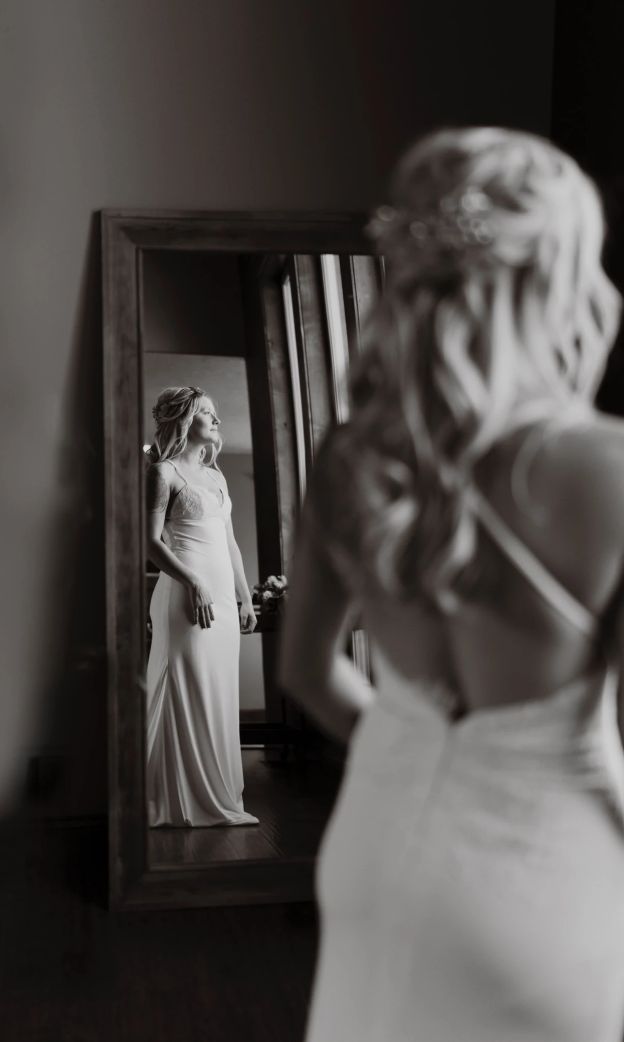 Black-and-white portrait of the bride looking into a full-length mirror before her wedding