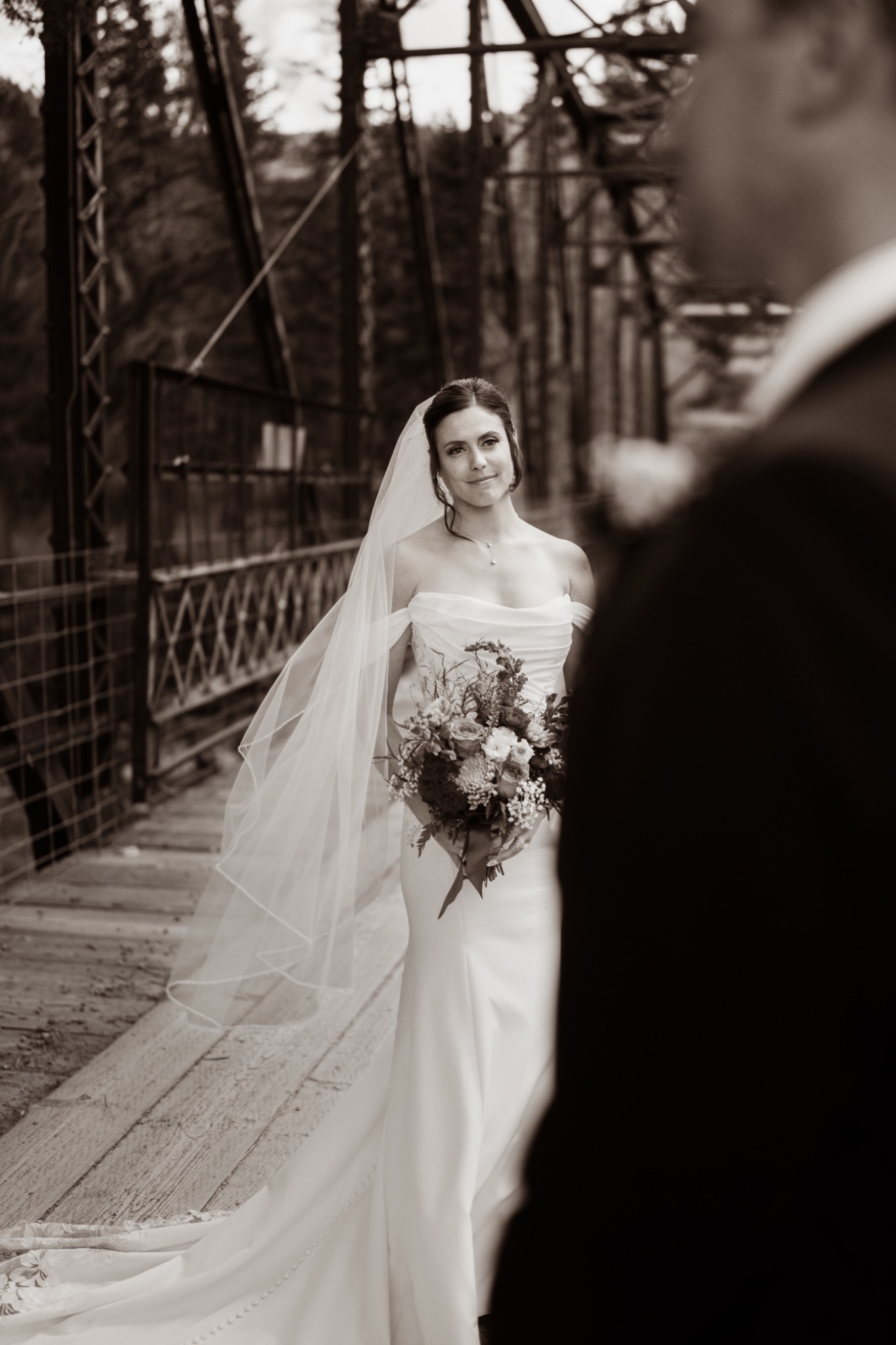 Black-and-white portrait of a bride holding her bouquet on a bridge