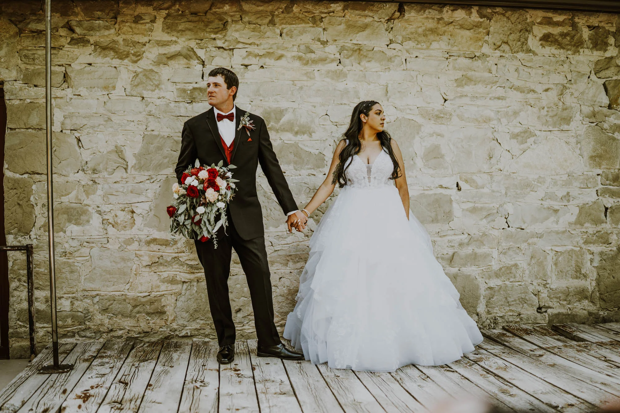 Bride and groom holding hands against a stone wall