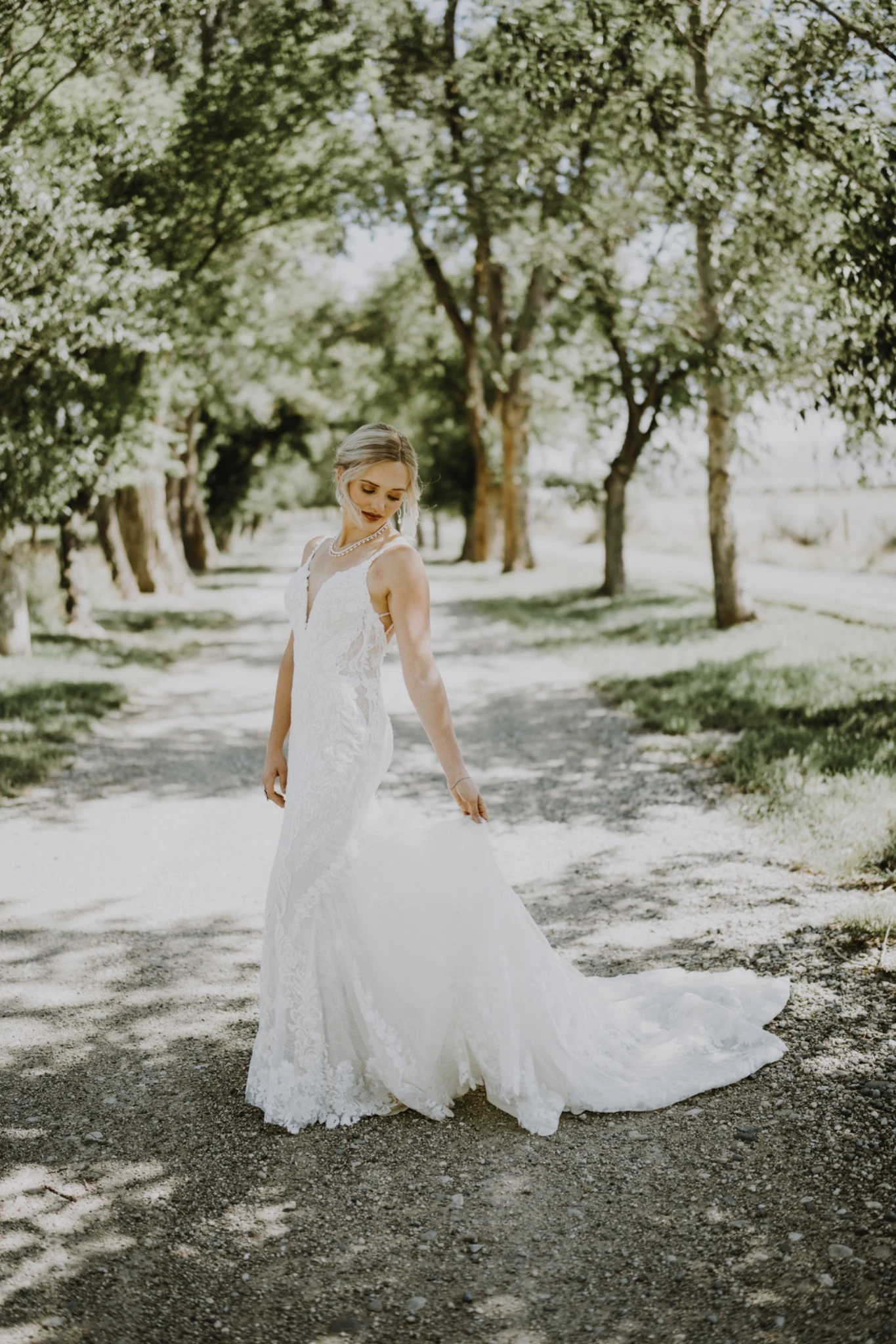 Bride standing beneath sunlit trees in her wedding dress