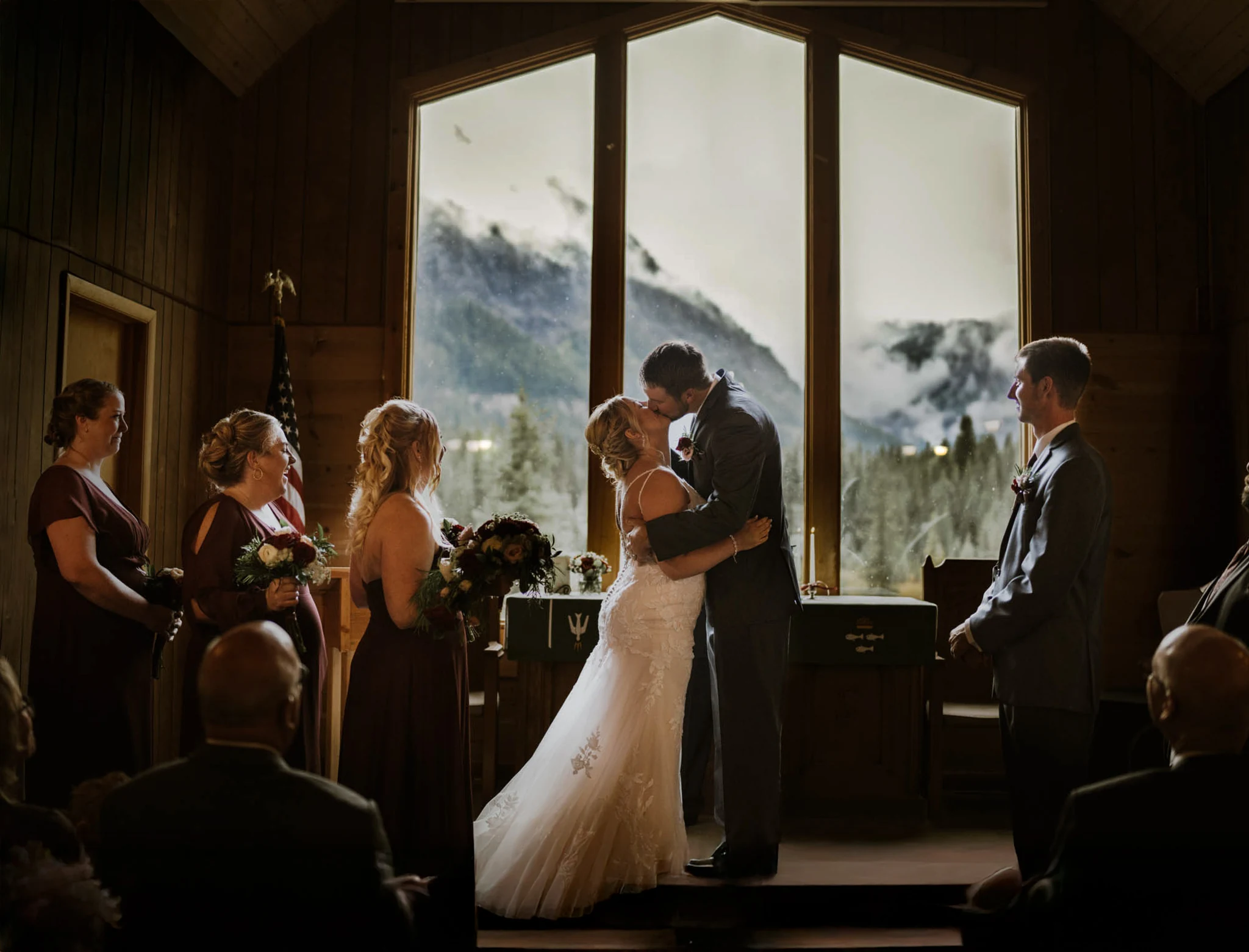 Couple kissing during their wedding ceremony in front of tall chapel windows