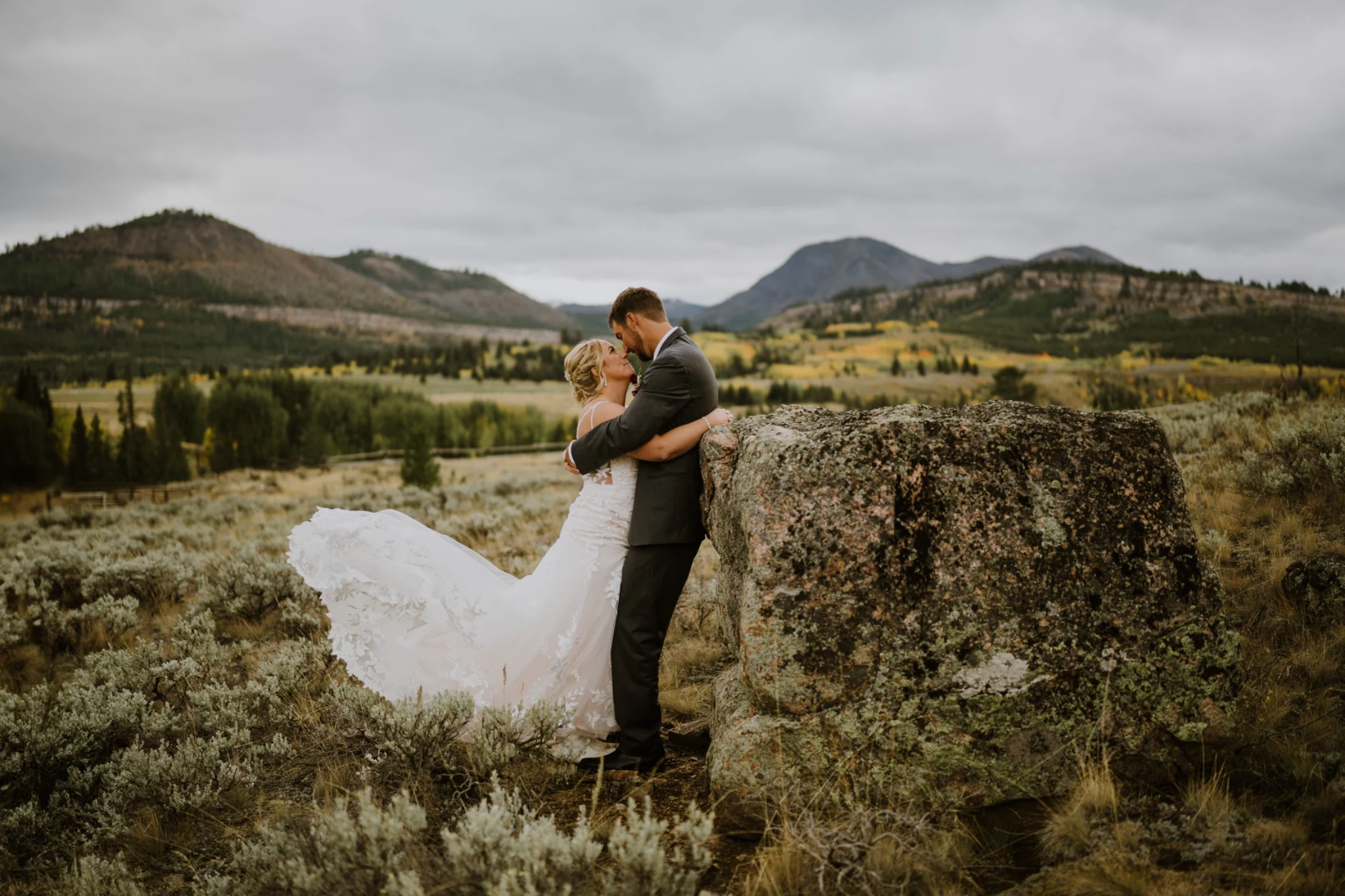 Couple kissing beside a boulder overlooking a mountain meadow