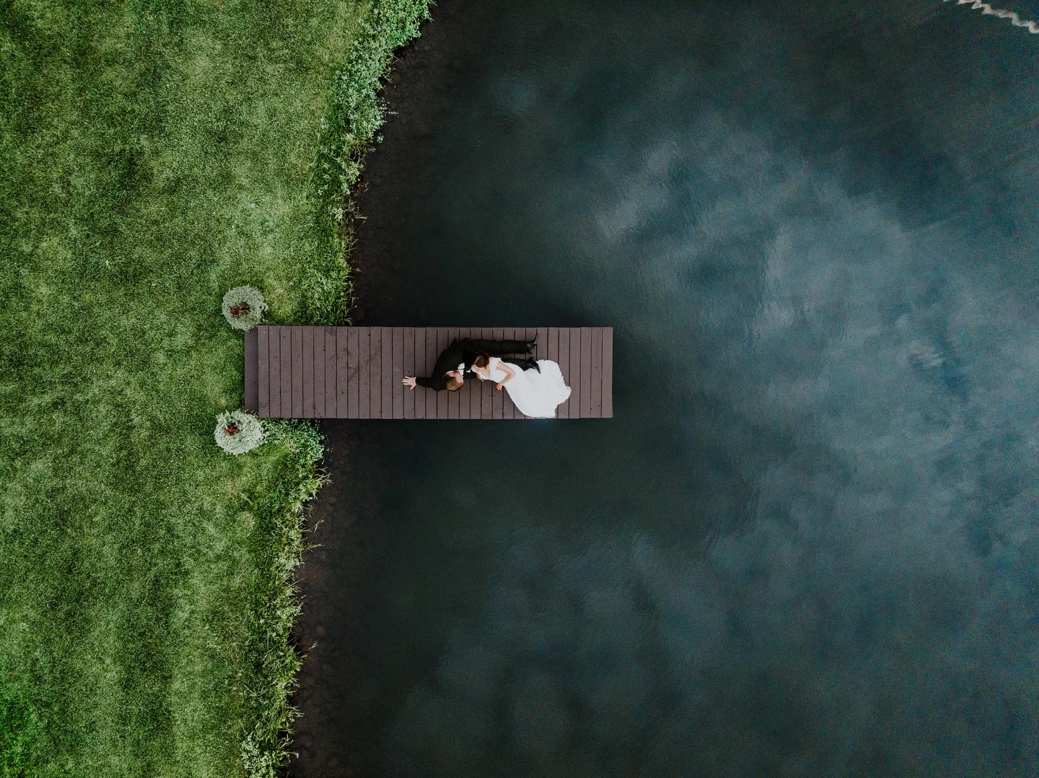 Aerial view of a newlywed couple on a wooden dock over dark water