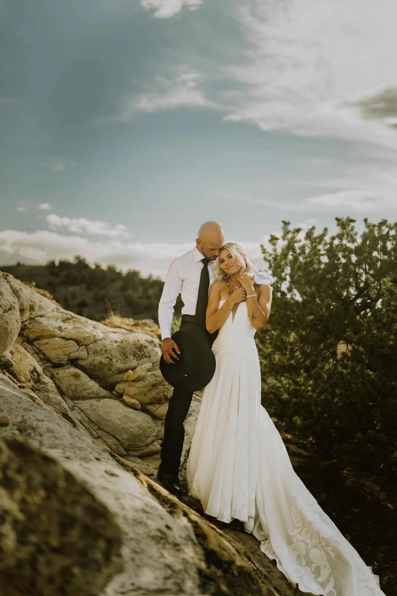 Bride and groom embracing on rocky terrain in evening light