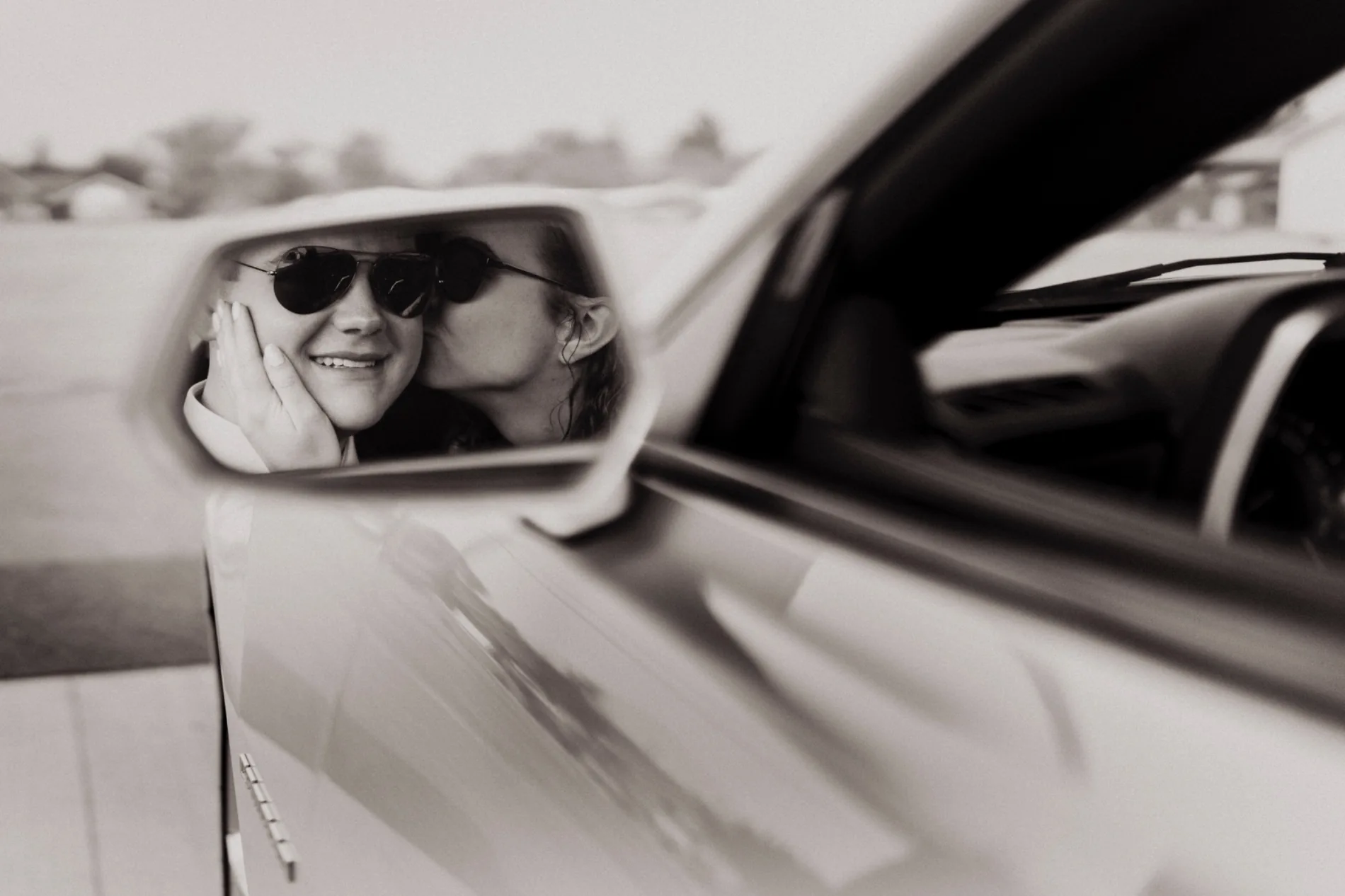 A wedding-day kiss reflected in a car mirror