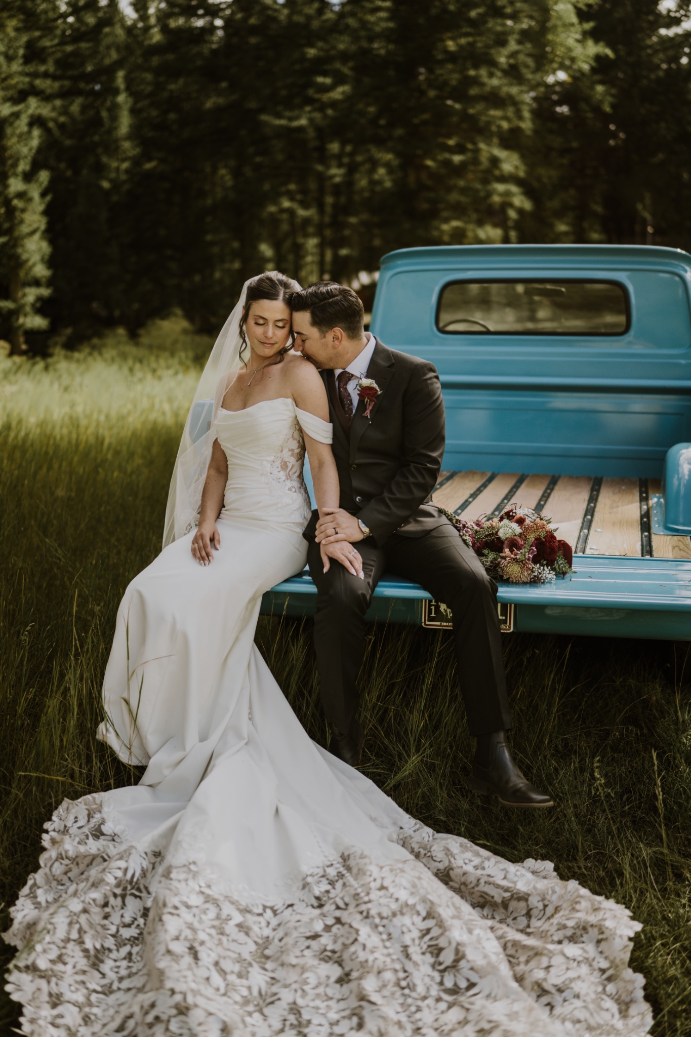Bride and groom sitting on the back of a turquoise truck in a forest